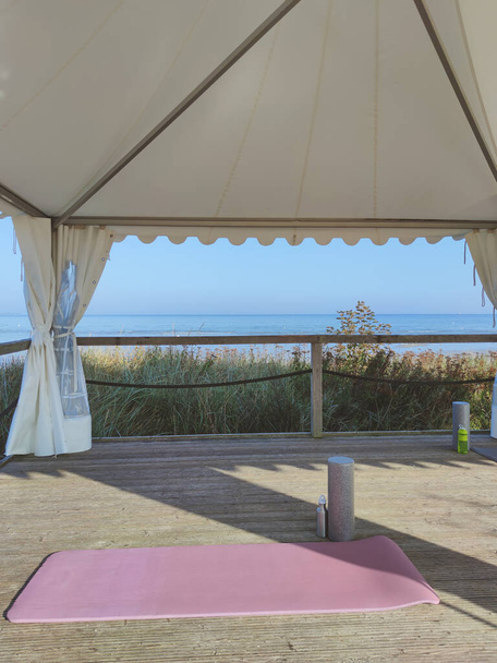 Photo of yoga mat and foam roller on wooden terrace outdoor with sea view in summer - Photo, image