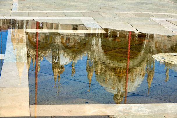 Basílica en la plaza San Marco de Venecia, reflejada en un charco después del final de la marea alta, o aqua alta, que inundó la plaza con agua de mar                                - Foto, Imagen