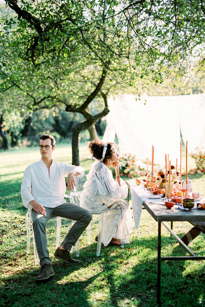 Man and woman are sitting on chairs near a laid table in a green garden - Foto, Imagem