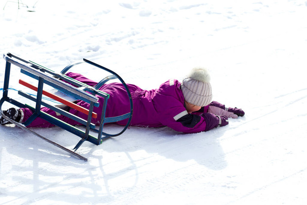 bambina su uno slittino luminoso giorno d'inverno nevoso. Il bambino è caduto dalla slitta rovesciata. Attività all'aperto invernali - Foto, immagini