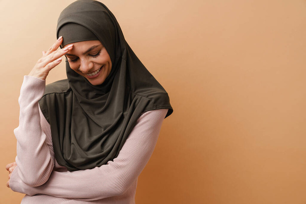 Mladá muslimka žena v šátku smích na kameru izolované přes béžové pozadí - Fotografie, Obrázek