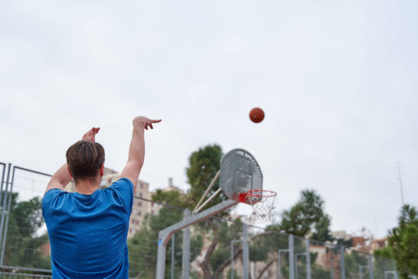 Kosárlabda játékos kék sportruházatban kosárba dobott egy kosárlabdát egy utcai kosárpályán.. - Fotó, kép