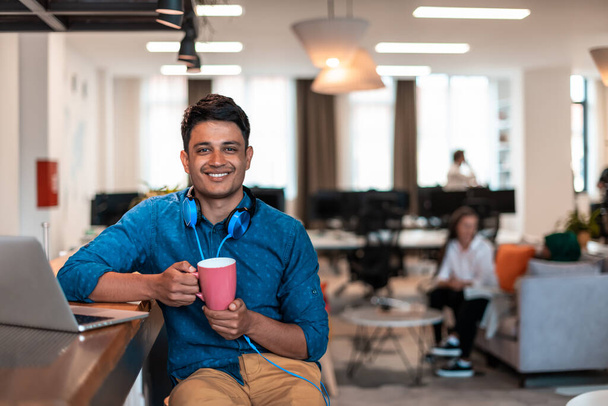 Casual businessman taking a break from the work using a laptop while drinking tea in relaxation area of modern open plan startup office. High-quality photo - Foto, Imagen