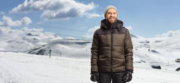 Young man in a winter jacket and pants standing on a snowy mountain - Valokuva, kuva