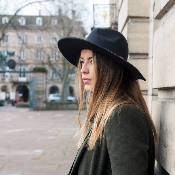 Portrait of young woman wearing a winter green coat and hat in the street - Photo, image