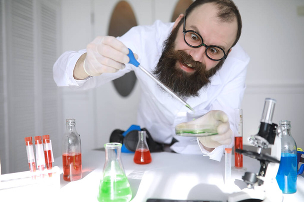 Chemicaliëngek. Een gekke wetenschapper voert experimenten uit in een wetenschappelijk laboratorium. Uitvoert onderzoek met behulp van een microscoop. - Foto, afbeelding