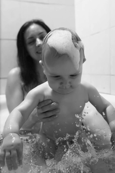 Anya mossa a gyerekeket. Anya és a gyerekek a fürdőszobában csinálják a vizes kezelést. Habszivacs, spray. - Fotó, kép