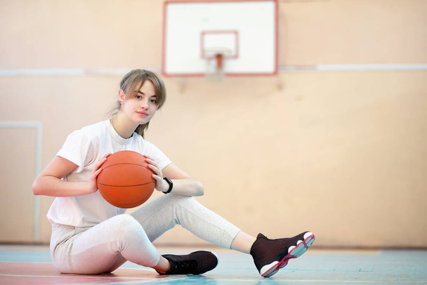 Девочка-студентка в спортзале играет в баскетбол - Фото, изображение