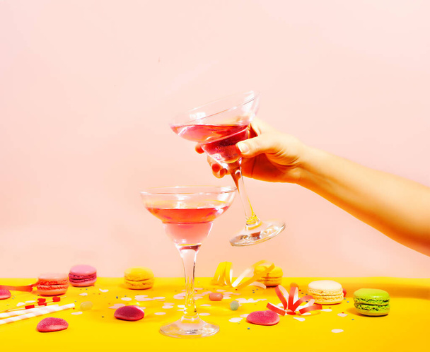 Glass of pink cocktail with heart candies and macaroons. Birthday party or Valentines day concept. Woman hand holding a glass. - Foto, Imagen