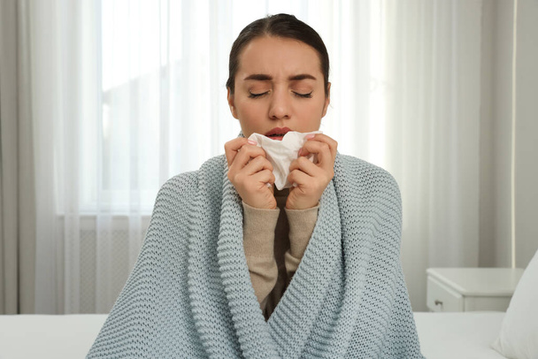 Sick young woman with tissue wrapped in knitted plaid at home - Foto, immagini