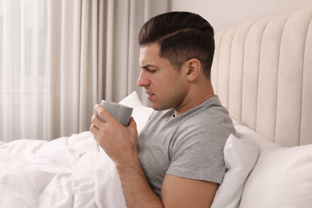 Sick man with cup of hot drink in bed at home - Foto, Bild