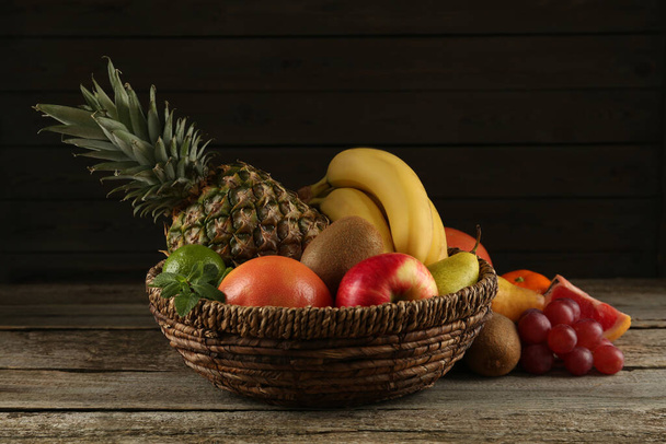 Fresh ripe fruits and wicker bowl on wooden table - Фото, зображення