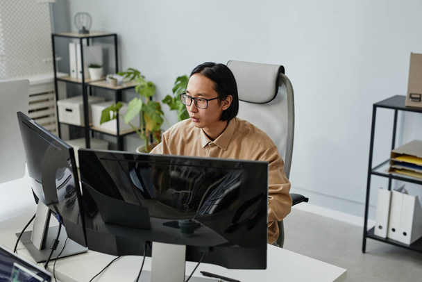 Asiatischer Geschäftsmann in Brille und lässiger Kleidung sitzt am Computermonitor - Foto, Bild