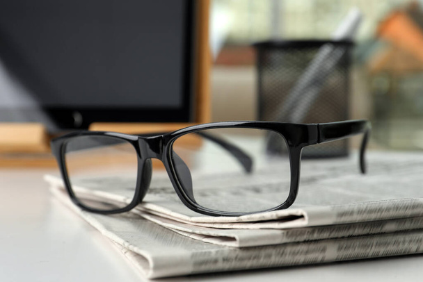 Стек газет і окулярів на білому столі в приміщенні, крупним планом
 - Фото, зображення