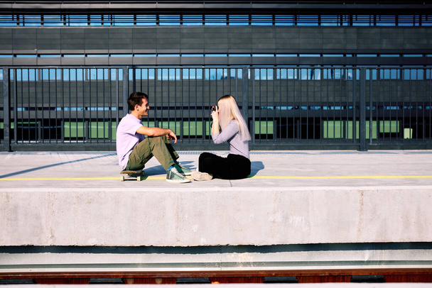 Una feliz pareja de adolescentes está sentada en la estación de tren y tomando fotos. - Foto, Imagen