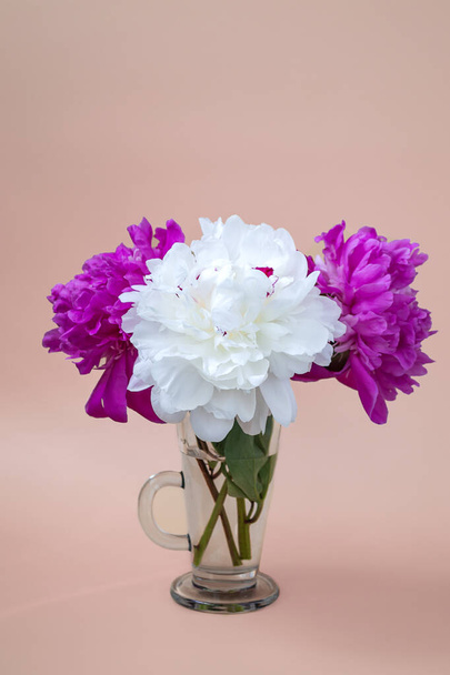 On a beige background, a bouquet of white and pink peonies in a glass. Close up, vertical format - Photo, image