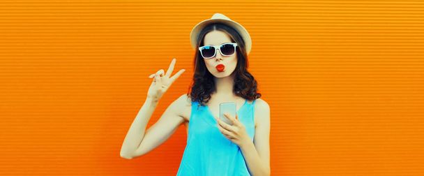 Portrait of caucasian young woman with smartphone wearing summer straw hat on orange background - Фото, зображення