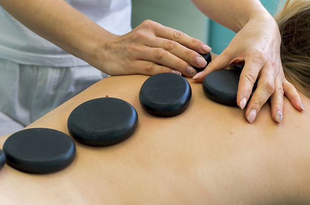 Stone therapy. Women's hands put hot basalt stones on their backs. Hot stone massage.Relaxation and spa treatments.Back and spine health.Massage room. - Photo, Image