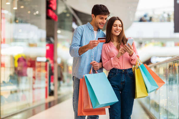 Glückliches Paar kauft mit Smartphone und Kreditkarte in Einkaufszentrum ein - Foto, Bild