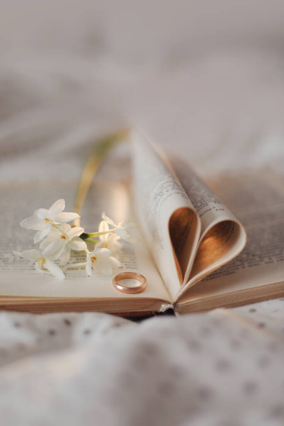 Goldener Hochzeitsring und aufgeschlagenes Buch mit gefalteten Blättern in Herzform. Hochzeitskonzept, Valentinstag - Foto, Bild