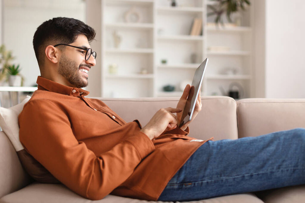 Lächelnder junger Araber mit digitalem Tablet zu Hause - Foto, Bild