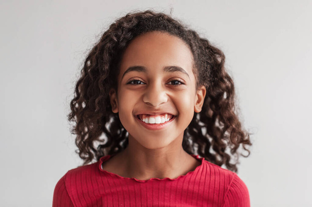 Kopfschuss eines lächelnden afroamerikanischen Mädchens posiert auf grauem Hintergrund - Foto, Bild