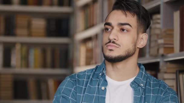 Harkitsevainen vakava huolissaan nuori latino mies opiskelija seisoo julkisessa yliopiston kirjastossa ajatellut tulevaisuuden tentit uusia ideoita mahdollisuuksia haluavat puolella tilalla leuka haaveilee syöksynyt ajatuksia - Materiaali, video