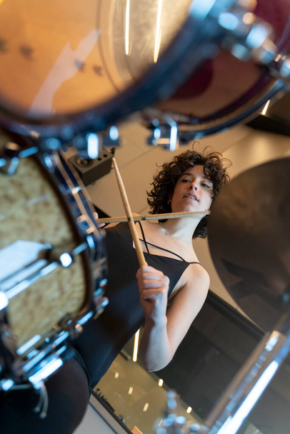 Junge Frau mit lockigem Haar spielt Schlagzeug in einem Tonstudio - Foto, Bild