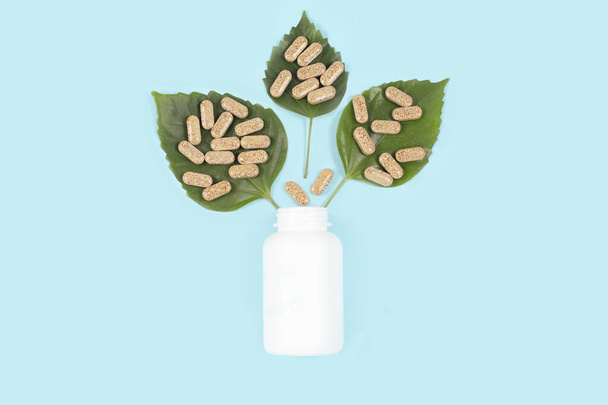 Pílulas orgânicas em folhas verdes e frasco no fundo azul - Foto, Imagem