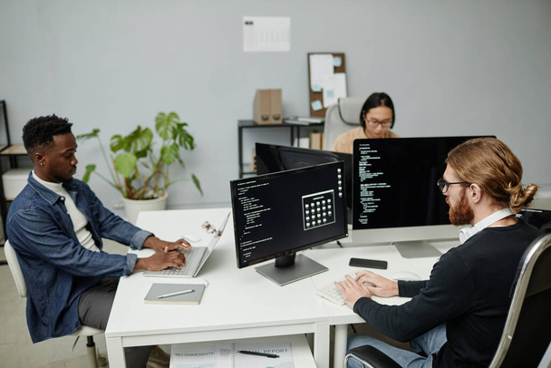 Grupo de ingenieros de software interculturales que trabajan frente a monitores de ordenador - Foto, Imagen