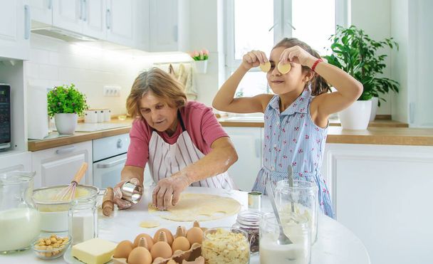 Kind en oma in de keuken bakt het deeg in de keuken. Selectieve focus. Voedsel. - Foto, afbeelding