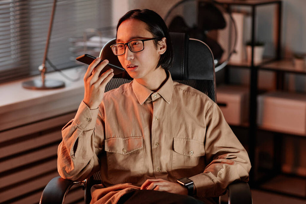 Молодой азиатский бизнесмен в очках и в повседневной рубашке записывает голосовое сообщение - Фото, изображение