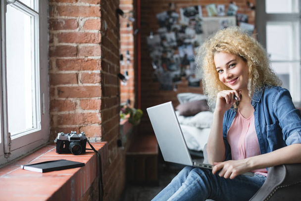 Happy smiling curly blonde woman working with laptop at home. - Fotoğraf, Görsel