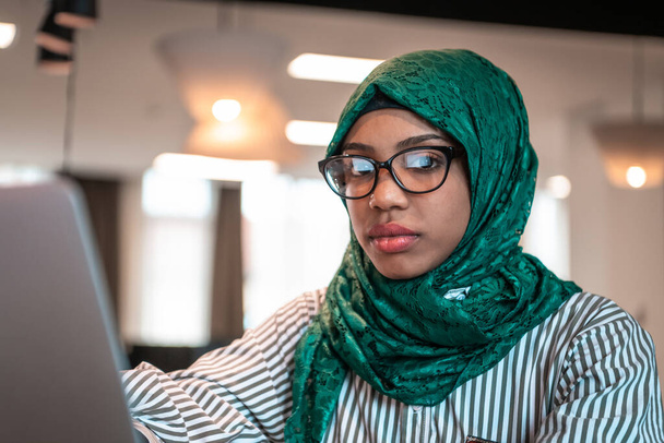Businesswoman wearing a green hijab using laptop in relaxation area at modern open plan startup office. Selective focus. High-quality photo - Foto, Imagem