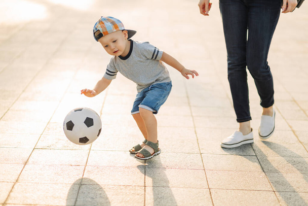 Мама і син грають у футбол разом на відкритому повітрі в парку, маленький хлопчик кидає м'яч у футбол, дитина вчиться грати в футбол. Родина грає в футбол разом у парку. - Фото, зображення
