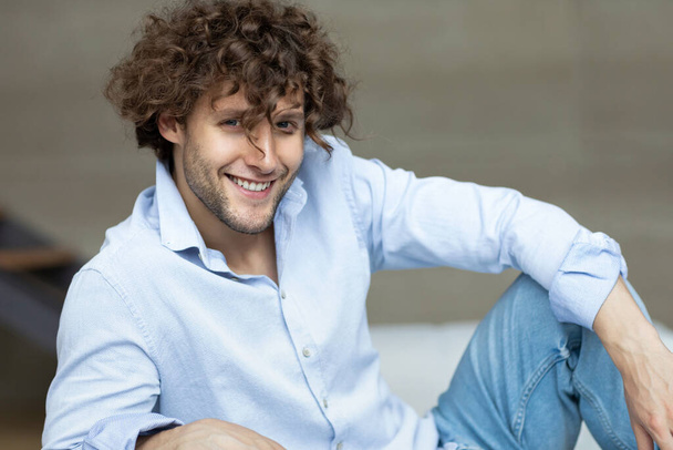 Close up shot of a handsome young curly haired man wearing a blue shirt indoors. - Foto, afbeelding