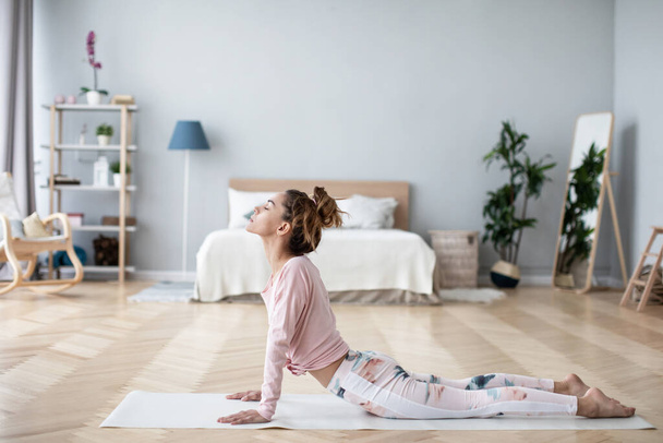 Attractive young woman working out in living room, doing yoga or pilates exercise on mat at home. - Fotografie, Obrázek