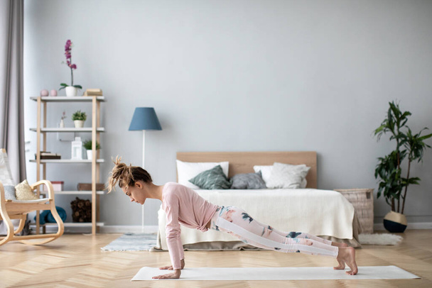 Young woman standing in plank pose or doing push-ups on yoga mat at home. Working out indoors. - Foto, Imagen