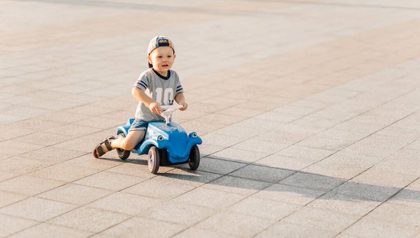Little boy rides on a toy car in the park, happy child on a sunny summer day, driving a car outdoors. The concept of childhood, entertainment, outdoor activities with children on a warm summer day. - Fotó, kép