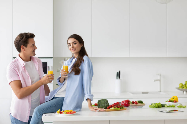 Healthy meal concept. Handsome man and woman with a glass of orange juice in the kitchen. Preparing a vegetarian salad with fresh vegetables. - Фото, зображення