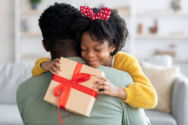Sorridente bambina nera che tiene la scatola regalo e abbraccia il papà - Foto, immagini