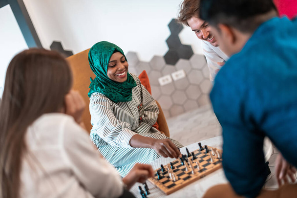 Multiethnic group of businesspeople playing chess while having a break in relaxation area at modern startup office. Selective focus. High-quality photo - Foto, afbeelding