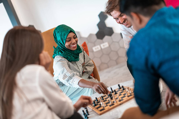 Multiethnic group of businesspeople playing chess while having a break in relaxation area at modern startup office. Selective focus. High-quality photo - Foto, afbeelding