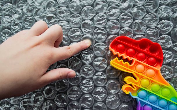 おもちゃはそれをポップ恐竜の虹色は、バブルラップの背景に多色の文字で-それをポップ。子供の指は泡を押して、ディノはそれを見てください。スペースのコピー. - 写真・画像