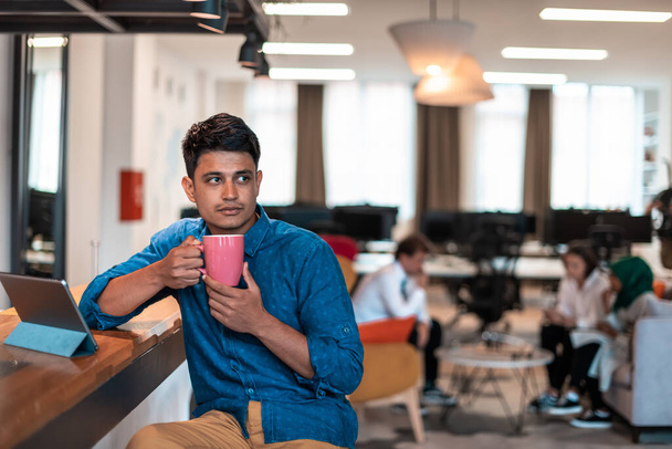 Casual businessman taking a break from the work using a laptop while drinking tea in relaxation area of modern open plan startup office. High-quality photo - Fotografie, Obrázek