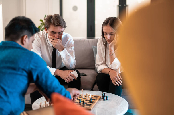 Multiethnic group of businesspeople playing chess while having a break in relaxation area at modern startup office. High-quality photo - Zdjęcie, obraz