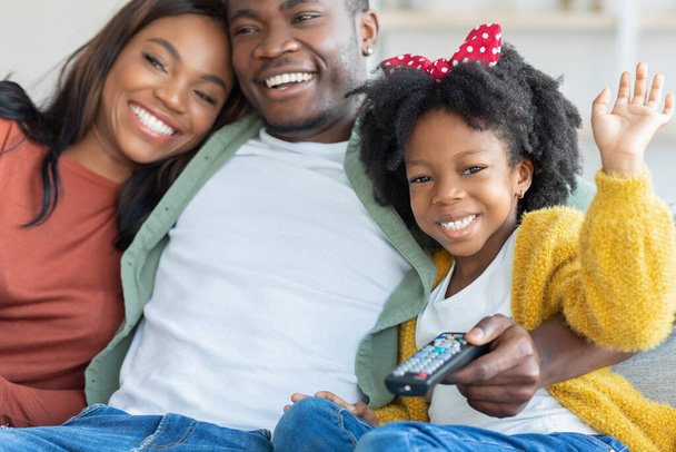 Jovens pais negros felizes e sua filhinha assistindo TV em casa - Foto, Imagem