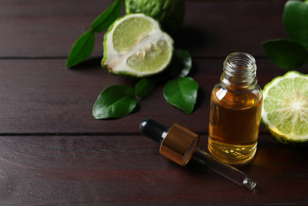 Bottle of essential oil, pipette and fresh bergamot fruit on wooden table. Space for text - Photo, image
