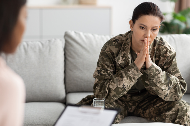 Deprimida mujer militar pensativa sentada en el sofá durante la sesión de terapia con el psicólogo - Foto, imagen