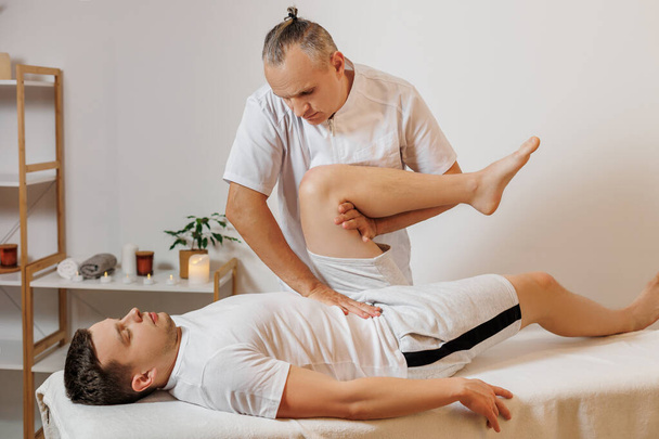 Strong and concentrated masseur therapist in uniform making manual therapy for sportsman. Professional massage back treatment. Alternative medicine. Concept of wellness, body and health care - Foto, Imagem